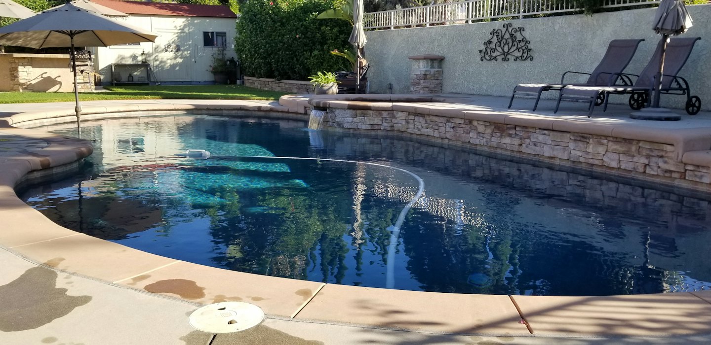 Pulitore robot per piscina in una piscina da giardino con cascata.