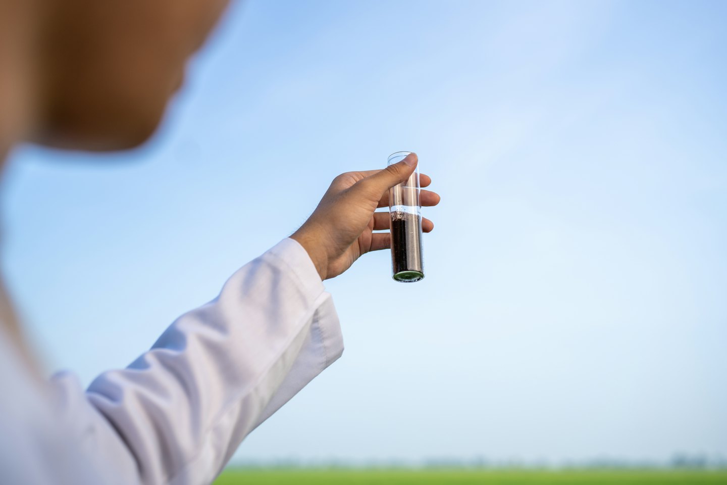 Scienziato esamina campione di terreno in provetta all'aperto.